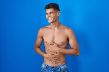 Young hispanic man standing shirtless over blue background with hand on stomach because indigestion, painful illness feeling unwell. ache concept. 