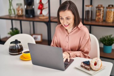 Middle age woman having breakfast using laptop sitting on table at home