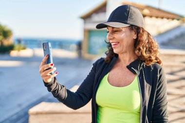 Orta yaşlı İspanyol kadın dışarıda akıllı telefonla çalışıyor.