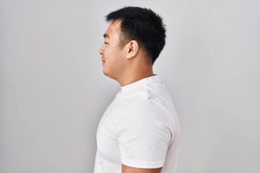 Young chinese man standing over white background looking to side, relax profile pose with natural face and confident smile. 