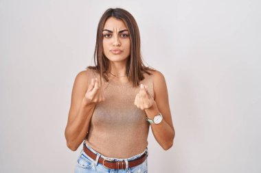 Young hispanic woman standing over white background doing money gesture with hands, asking for salary payment, millionaire business 
