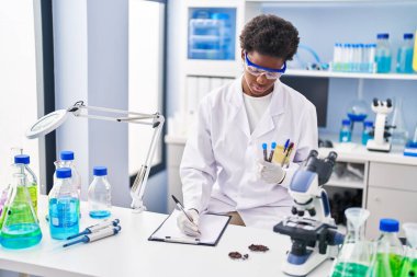 Bilim adamı üniforması giyen Afrikalı Amerikalı bir kadın laboratuarda elinde test tüpleriyle panoya yazı yazıyor.