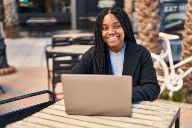 Kahve dükkanının terasında dizüstü bilgisayar kullanan Afrikalı Amerikalı kadın.