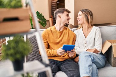 Young man and woman couple using touchpad sitting on sofa at new home