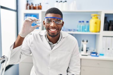 Laboratuvarda elmas tutan, bilim adamı üniforması giyen genç Afrikalı Amerikalı.