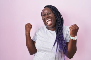 Young african woman standing over pink background celebrating surprised and amazed for success with arms raised and eyes closed. winner concept. 