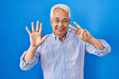Hispanic senior man wearing glasses showing and pointing up with fingers number eight while smiling confident and happy. 