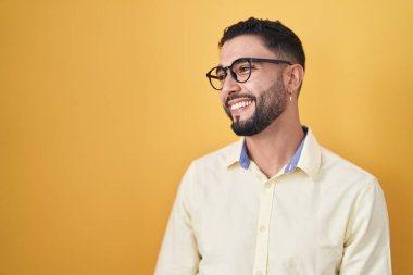Hispanic young man wearing business clothes and glasses looking away to side with smile on face, natural expression. laughing confident. 