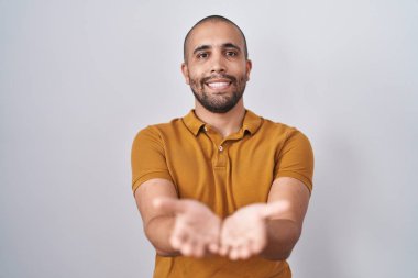 Hispanic man with beard standing over white background smiling with hands palms together receiving or giving gesture. hold and protection 