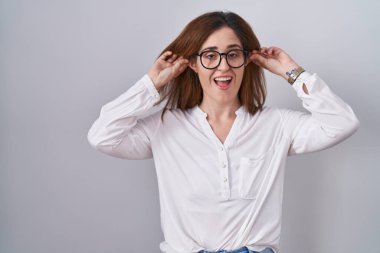 Esmer kadın izole edilmiş beyaz arka planda gülümsüyor kulakları parmaklarıyla çekiyor, komik bir jest. deneme sorunu 