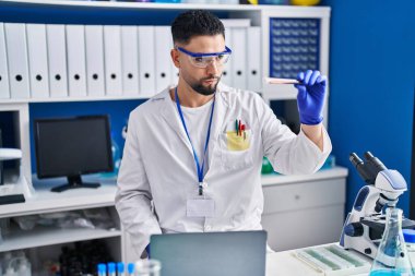 Young arab man scientist using laptop holding blood analysis test tube at laboratory
