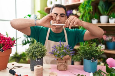 Young hispanic man florist make photo to lavender plant by smartphone at flower shop
