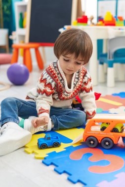 Adorable toddler playing with car toy sitting on floor at kindergarten