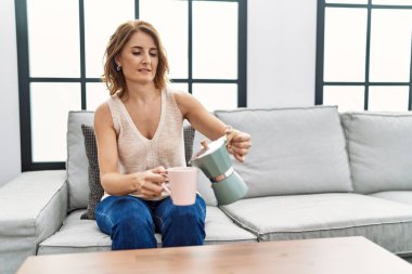 Orta yaşlı İspanyol kadın gülümseyerek evde kahve içiyor.