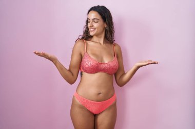 Young hispanic woman wearing lingerie over pink background smiling showing both hands open palms, presenting and advertising comparison and balance 