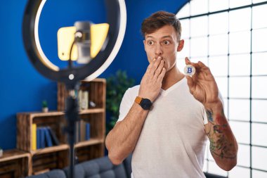 Beyaz adam evde akıllı telefonla Bitcoin dersi kaydediyor ağzını eliyle kapatıyor, şok geçiriyor ve hata yapmaktan korkuyor. şaşırmış ifade 