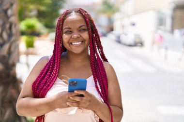 Afro-Amerikalı kadın sokakta akıllı telefon kullanarak kendine güveniyor.