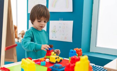 Adorable toddler playing with construction blocks standing at kindergarten