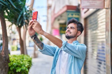 Genç İspanyol adam gülümsüyor. Sokakta akıllı telefonun yanında özçekim yapıyor.
