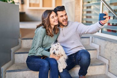 Man and woman holding dog making selfie by the smartphone at street
