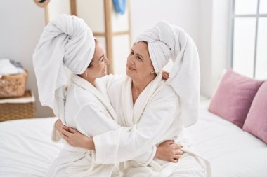 Mother and daughter wearing bathrobe hugging each other at bedroom