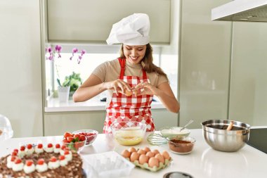 Young beautiful hispanic woman smiling confident pouring egg on bowl at the kitchen