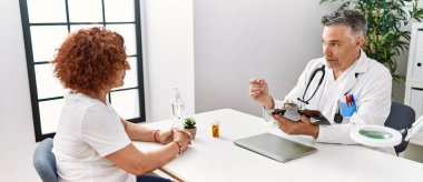 Doktor üniforması giyen orta yaşlı bir adam ve kadın klinikte tıbbi danışmanlık yapıyorlar.