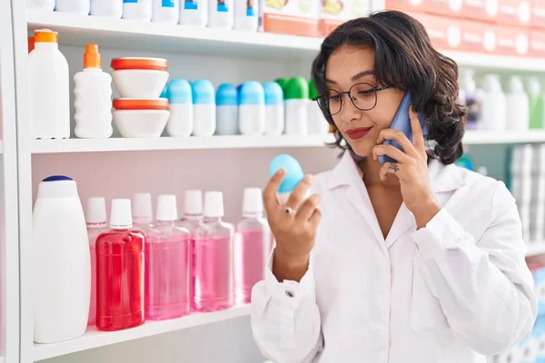 Young Beautiful Hispanic Woman Pharmacist Talking Smartphone Holding Deodorant Pharmacy — Zdjęcie stockowe