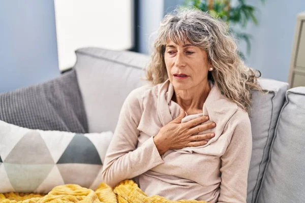 Middle age woman suffering for chest pain sitting on sofa at home