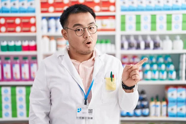 薬局で働く中国の若者ドラッグストア驚きを指して指で側面に 口を開けて驚いた表情 — ストック写真