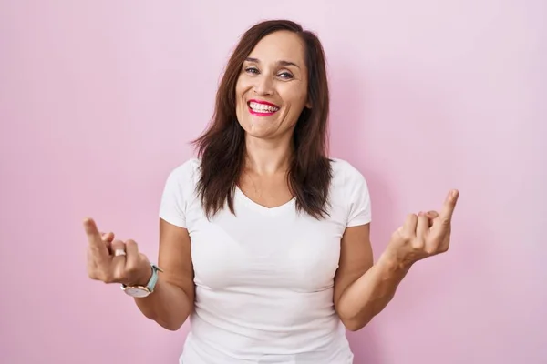 Middle age brunette woman standing over pink background showing middle finger doing fuck you bad expression, provocation and rude attitude. screaming excited