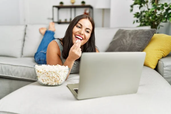 Young beautiful hispanic woman watching movie eating popcorn at home