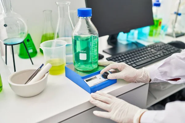 Middle age hispanic woman wearing scientist measuring liquid at laboratory
