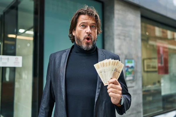 英俊的中年男子 手里拿着100枚丹麦克朗钞票 惊慌失措 张大了嘴 满脸诧异 — 图库照片