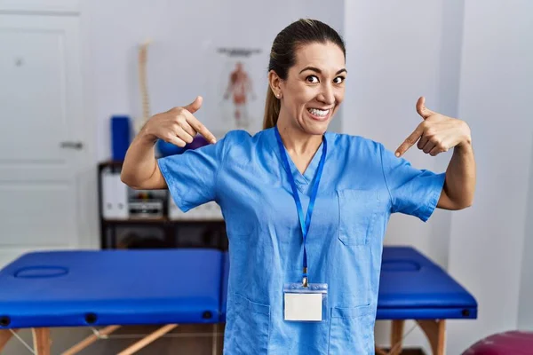 Mladá Hispánka Uniformě Fyzioterapeutky Stojící Klinice Sebevědomě Usmívající Ukazující Prstem — Stock fotografie