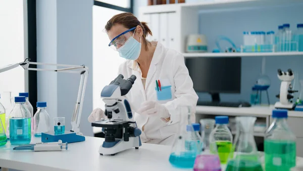 实验室显微镜下穿着科学家制服和医疗面具的中年恐慌女性 — 图库照片