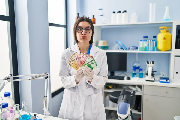 科学研究所で働いている若いヒスパニック系の女性は お金の銀行券を持っている面白い顔で頬をパフ 空気を吸い込み空気を吸い込み — ストック写真