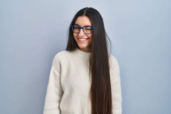 Young Hispanic Woman Wearing Casual Sweater Blue Background Winking Looking —  Fotos de Stock