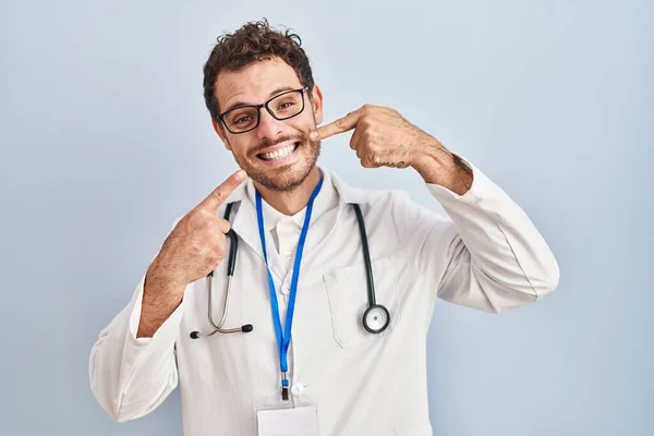 医者の制服を着た若いヒスパニック系の男と 明るい表情と指の歯と口で指して笑顔聴診器 歯の健康の概念 — ストック写真