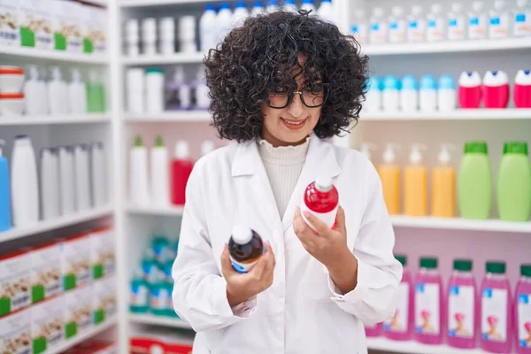 Young middle eastern woman pharmacist smiling confident holding medication bottles at pharmacy