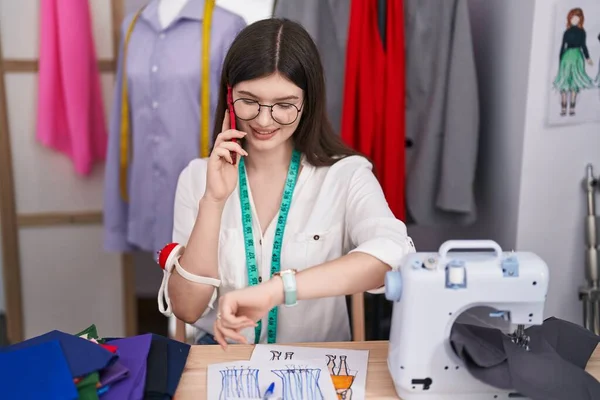 年轻的高加索女人裁缝用智能手机说话 看着裁缝店的手表 — 图库照片