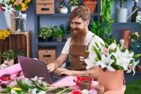 Young redhead man florist smiling confident using laptop at flower shop