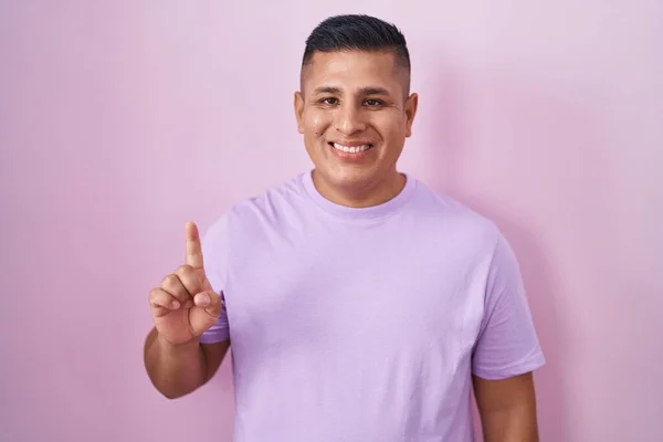 Mladý Hispánec Stojící Nad Růžovým Pozadím Ukazující Ukazující Prstem Číslo — Stock fotografie