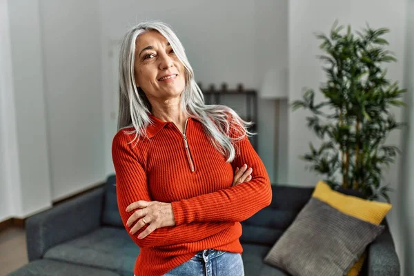Middle age grey-haired woman smiling confident standing with arms crossed gesture at home