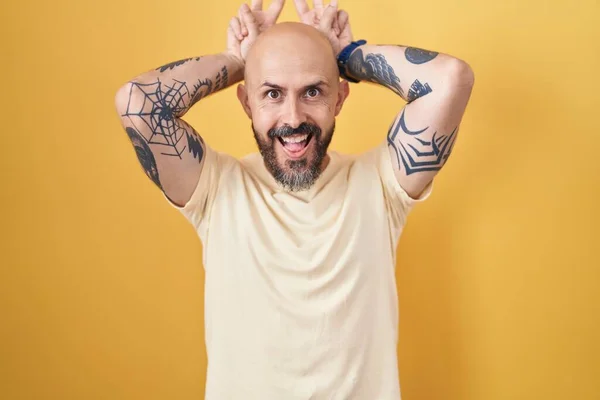 Латиноамериканец Татуировками Стоящий Желтом Фоне Изображающий Смешного Сумасшедшего Пальцами Голове — стоковое фото