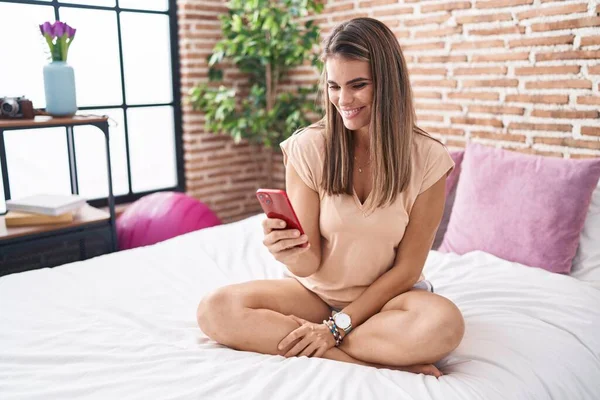 年轻美丽的惊慌失措的女人坐在卧室的床上用智能手机 — 图库照片