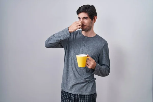 Young Hispanic Man Wearing Pajama Drinking Cup Coffee Smelling Something — Stockfoto