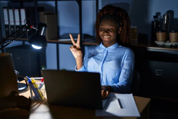 African woman working at the office at night showing and pointing up with fingers number two while smiling confident and happy.