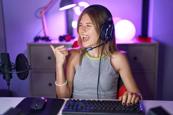 Blonde Caucasian Woman Playing Video Games Headphones Pointing Thumb Side — стоковое фото