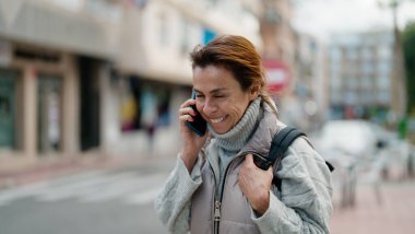 Orta yaşlı İspanyol kadın gülümsüyor. Akıllı telefondan konuşuyor.